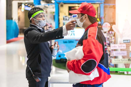 KANCHANABURI, THAILAND - APRIL 28,2020: Unidentified male officer use thermometer scan temperature for fever in people as coronavirus or COVID-19 outbreak at Robinson Department Store.のeditorial素材