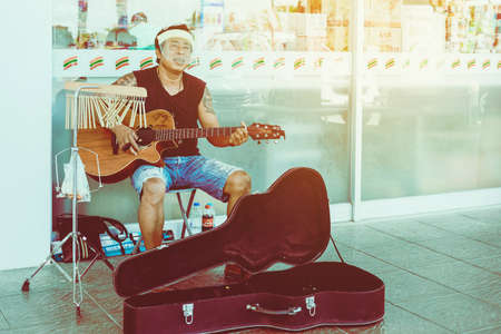 KANCHANABURI,THAILAND-APRIL 18,2020: Unidentified street musician wear a face mask playing guitar and tubular bells in front of 7-Eleven at Thamuang district on april 18,2020 in Kanchanaburi,Thailand.のeditorial素材