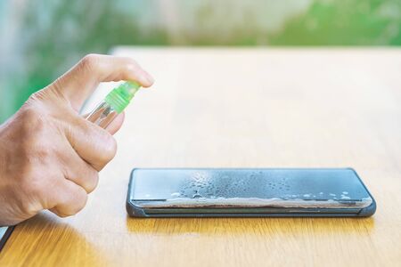Hands of woman cleaning smartphone with alcohol spray to prevent infection of corona virus...