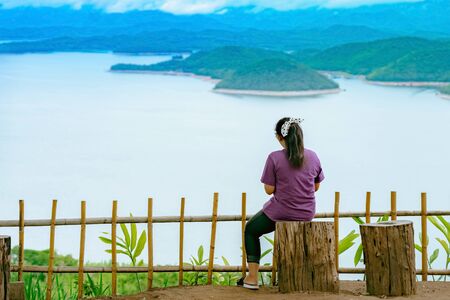 Back view of woman enjoy with beautiful scenery view of nature with a large reservoir above the Srinagarind Dam at Rai Ya Yam view point in Si Sawat District, Kanchanaburi Thailand.の写真素材