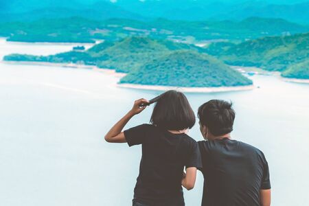Back view of lovers enjoy with beautiful scenery view of nature with a large reservoir above the Srinagarind Dam at Rai Ya Yam view point in Si Sawat District, Kanchanaburi Thailand.の写真素材
