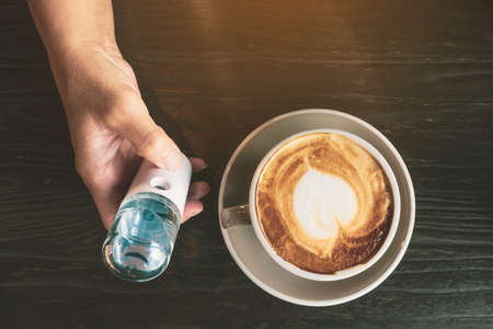 Hand holding hand sanitizer with a cup of coffee on wooden tableの写真素材