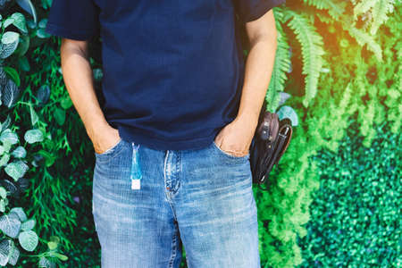 portable alcohol gel bottle to kill Corona Virus(Covid-19) hanging on belt loop of man' s jeans with plants background. New normal lifestyle. Health care concept. Selective focus on alcohol gelの写真素材