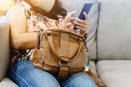 Mini portable alcohol gel bottle to kill Corona Virus(Covid-19) hang on a brown leather shoulder bag on table in coffee shop.New normal lifestyle. Health care concept. Selective focus on alcohol gelの写真素材