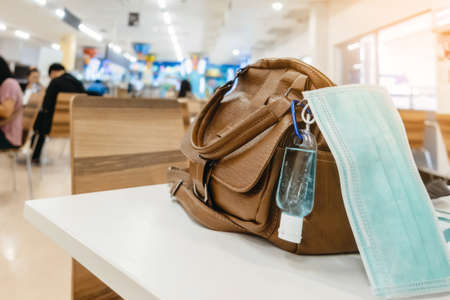 Mini alcohol gel bottle to kill Corona Virus(Covid-19) hang on a brown leather shoulder bag with hot coffee on table in cafe.New normal lifestyle.Health care concept.Selective focus on alcohol gelの写真素材