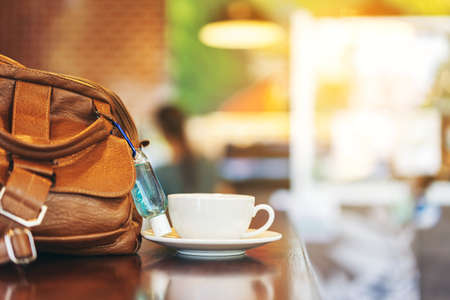 Mini portable alcohol gel bottle to kill Corona Virus(Covid-19) hang on a brown leather shoulder bag on table in garden. New normal lifestyle. Health care concept. Selective focus on alcohol gelの写真素材