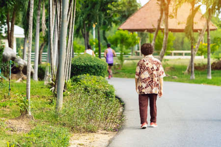 Back view portrait of a Asian elderly man in fitness wear walking and jogging for good health in public park. Senior jogger in nature.  Older Man enjoying Peaceful nature. Healthcare concept.の写真素材