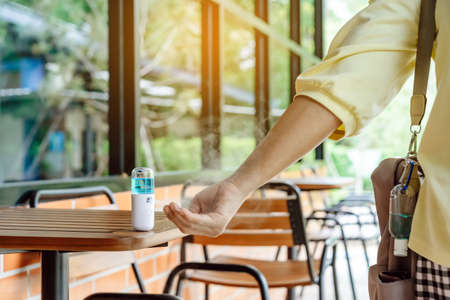 Mini portable alcohol gel bottle to kill Corona Virus(Covid-19) hang on a brown leather shoulder bag on table in coffee shop.New normal lifestyle. Health care concept. Selective focus on alcohol gelの写真素材