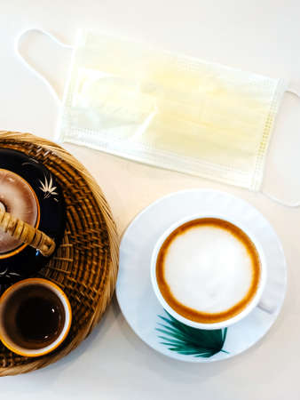 Hot Cappuccino coffee with protective mask on a wooden table for people being quarantined in the...