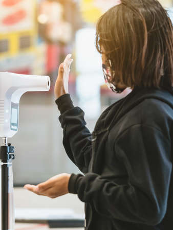 Customer with protective mask raised hand at digital thermometer with temperature scanning machine...