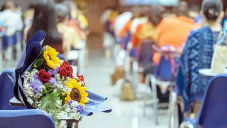 Beautiful sunflowers with bouquet on a chair set for social distancing in auditorium. Congratulation concept in coronavirus pandemic.  Celebration in meeting room. Selective focus on sunflowersの写真素材