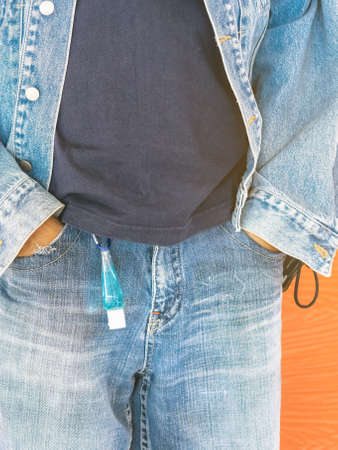 Mini portable alcohol gel bottle to kill  Virus  hanging on belt loop of man' s jeans with plank background. New normal lifestyle. Health care concept. Selective focus on alcohol gelの写真素材