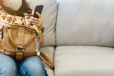 Mini portable alcohol gel bottle to kill  Virus hang on a brown leather shoulder bag on sofa in coffee shop.New normal lifestyle. Health care concept. Selective focus on alcohol gelの写真素材