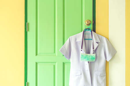 New surgical mask to prevent the spread of  Virus  hanging with the nurse's uniform on a hanger on a door knob in front of bedroom. New normal lifestyle before go to work concept.の写真素材