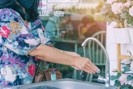 A woman wear protective face mask washing her hands with water from the tap in a aluminium tub. Concepts of Flu virus . New normal lifestyle. Selective focus on hand.の写真素材