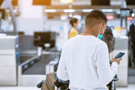 Back view of airline passenger wear face mask to prevent Corona virus (Covid-19) wait to check in counter in airport with staff wear face mask. New normal concept of travel after Covid-19 pandemic.の写真素材