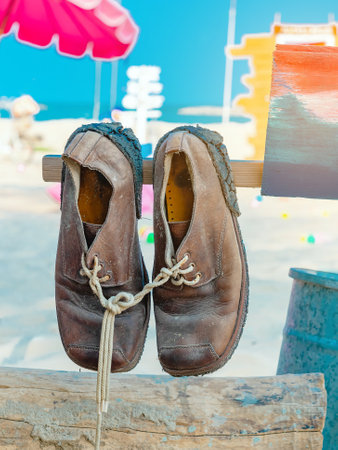 Pair of old brown leather shoes tied together with shoelaces hanging at the old vintage wooden pole...
