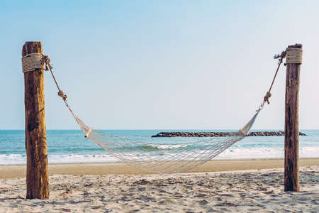 Empty cozy hammock made of mesh hang on wooden poles on the tropical white beach for tourists....