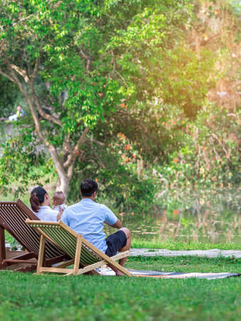 Back view of Asian lover with baby sit to relax on garden chair and by the table in garden.Summer vacation in green surroundings.Happy person outdoors relaxing on deck chair in garden.Outdoor leisure.の写真素材