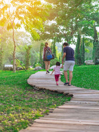 Back view of Asian Father hand holding lovely daughter walking on pathway through green garden.Dad and daughter walking together in park. Happy family spending time together outside in green nature.の写真素材