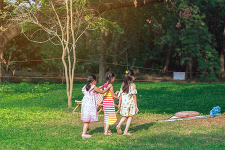 Asian girls and friends playing together on lawn through green garden. Happiness girl friends having fun on field among trees and green grass. Happy friends spending time outside in green nature.の写真素材