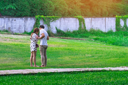 Back view of Asian lovers with camera relaxing in garden. Summer vacation in green surroundings. Happy couple spending time together outside in green nature. Enjoying nature outdoors. Outdoor leisure.の写真素材