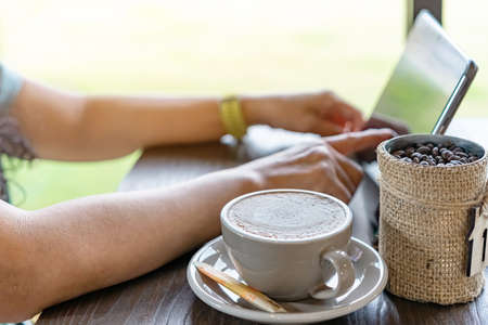 Hot Cappuccino coffee for quarantined woman wear face mask and work from home by using tablet and stress relief with hot coffee. Concepts of Covid-19 (Coronavirus disease). Selective focus on coffee.の写真素材