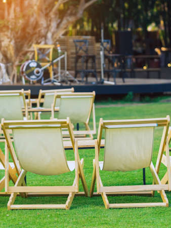 Many empty white deck chairs with tables in lawn is surrounded by shady green grass. Comfortable on outdoor patio chairs in garden.  Lawn chairs in the park. Sunbeds in the garden. Selective focus.の写真素材