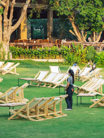 KANCHANABURI, THAILAND-FEBRUARY 3,2021 : Unidentified waitress wears face mask to prevent COVID-19 stand by to serve customers among many deck chairs on the lawn at The village farm to cafe restaurantのeditorial素材