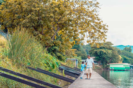KANCHANABURI, THAILAND-SEPTEMBER 5,2020 : Unidentified Asian grandfather and grandchild wear protective face mask to prevent Coronavirus (COVID-19) walking on wooden bridge along river at Din Cafe.のeditorial素材