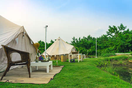 Holiday tents and lounge areas on green lawn place among trees at natural parkland. Camping tent on...