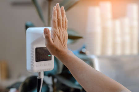 Customer raised hand at digital thermometer with temperature scanning machine for fever before...