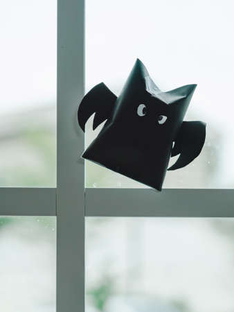 Origami bat made of black paper, isolated on glass window or door background. Dark paper ghost Halloween party concept origami paper bat. The figure of black paper bat flying over white background.の写真素材