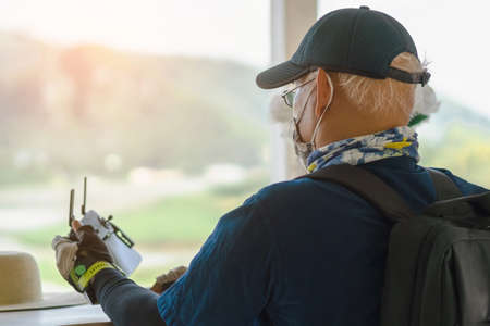 Back view of Asian old male engineer doing inspection using drone while wear face mask to avoid...