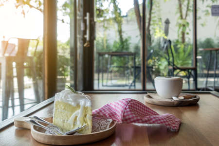 Delicious Coconut cake for breakfast and protective face mask place on the wooden table during covid-19 pandemic with blurred image of coffee cup in background. Health care concept. Selective focus.の写真素材