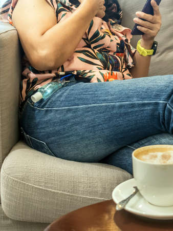 Mini portable alcohol gel bottle to kill Corona Virus(Covid-19) hanging on belt loop of woman' s jeans with hot coffee on table.New normal lifestyle.Health care concept.Selective focus on alcohol gel.の写真素材