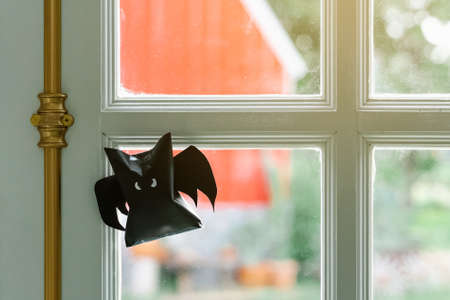 Origami bat made of black paper, isolated on glass window or door background. Dark paper ghost Halloween party concept origami paper bat. The figure of black paper bat flying over white background.の写真素材