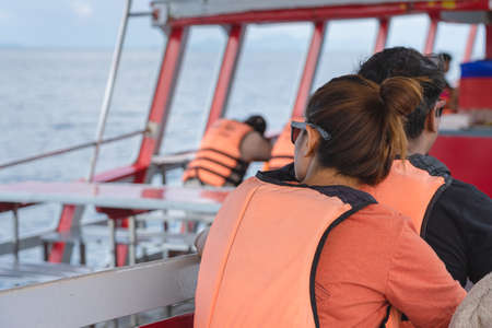 Back view of lover passengers in life vest relaxing on balcony enjoying view from boat of Samui island in sea.Happy casual couple tourists outside on tropical holiday destination.Cruise ship vacation.の写真素材