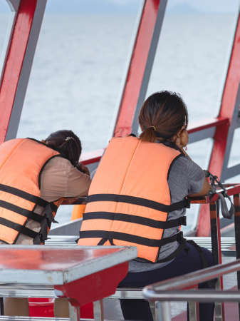 Back view of Asian woman in life vest relaxing on balcony enjoying view from boat of Samui island in the sea. Happy casual female tourists outside on tropical holiday destination.Cruise ship vacation.の写真素材