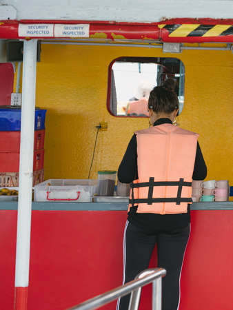 Back view of woman prepare refreshments and snacks while relaxing on balcony from boat of Samui island in sea.Happy casual female tourists outside on tropical holiday destination.Cruise ship vacation.の写真素材