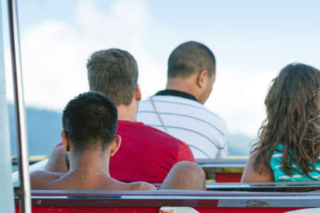 Back view of male passengers relaxing on balcony enjoying view from boat of Samui island in the sea....