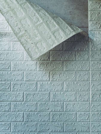 The wallpaper begins to peel off. Old white bricks wallpaper peeled off from the wall inside the room due to moisture or poor quality gluing. Repair and construction services concept. Selective Focus.の写真素材