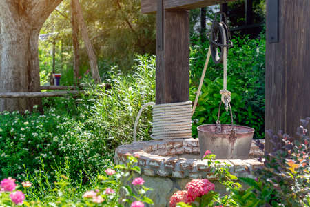 Beautiful artesian well made by stones and wheel pulley with metal bucket and rope in peaceful garden atmosphere. Retro stone water well in rural area. Garden decoration with antique items.の写真素材