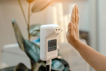 Customer raised hand at digital thermometer with temperature scanning machine for fever before...