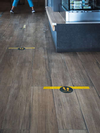 STAND HERE foot sign or symbol on wooden floor in coffee shop. Coffee shop set foot sign for social distancing to order coffee and wait to take home. Concept of keep distance, New normal lifestyle.の写真素材