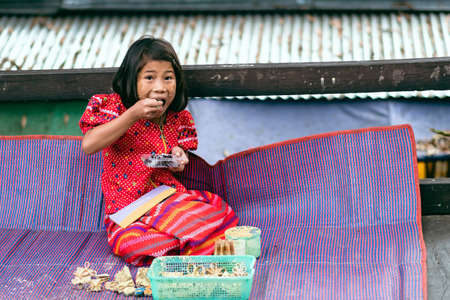 KANCHANABURI THAILAND-DECEMBER 31,2019 : Unidentified Mon girl eating dessert while sells flowers and make tanaka powdering service to tourists on Uttamanusorn wooden bridge at Sangkhlaburi.のeditorial素材