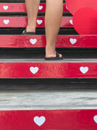 Feet of young woman walk up the stairs decorated with beautiful red and white hearts on occasion of Valentines Day festival of love. Wedding theme and Valentines Day concept. Selective focus on feet.の写真素材