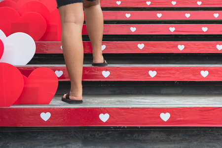 Young woman feet walking up stairs with beautiful red and white heart shape made from corrugated...