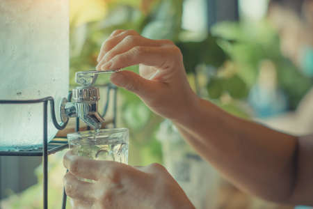 Hand of thirsty woman press the drinking cool water into a clear glass. Female finger pressing a...