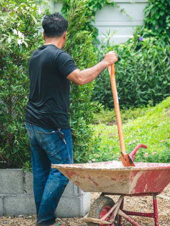 Asian professional gardener use shovels to prepare soil on wheelbarrows for planting ornamental plants in garden. Farmer with shovel in his hands. Outdoor work concept. Planting and decorate the park.の写真素材